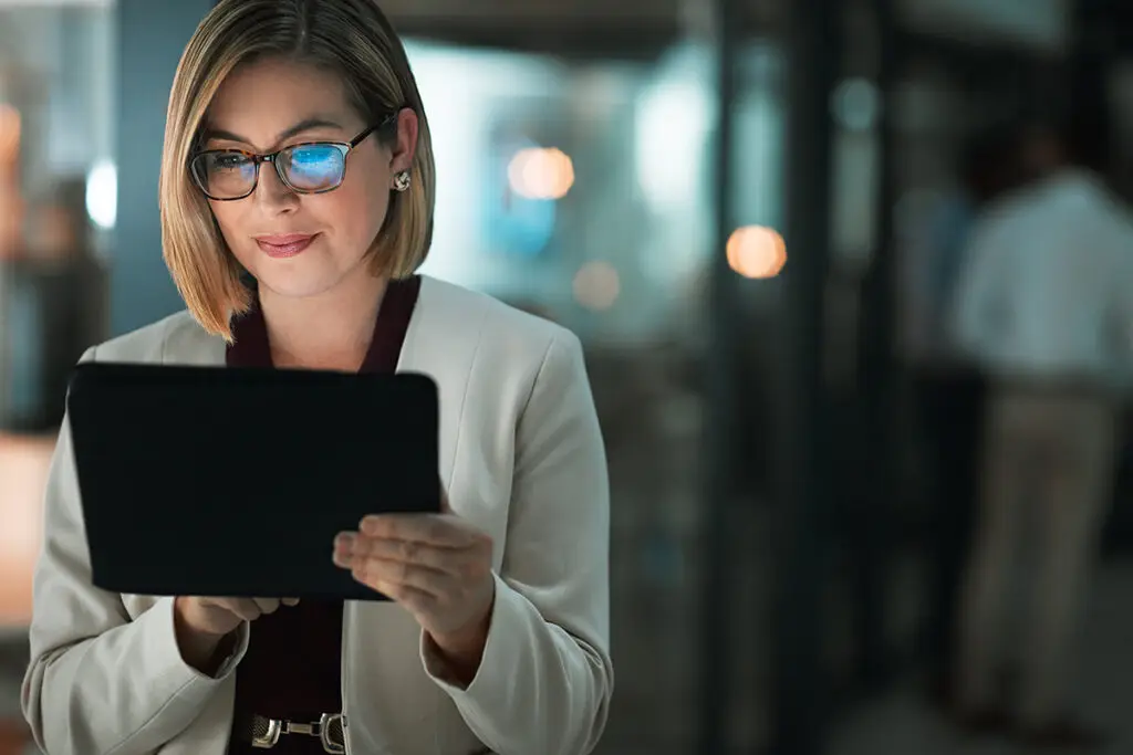 woman holding tablet in dark office with glare of screen in glasses